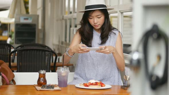 A young Asian woman takes a photo pancake at a cafe.