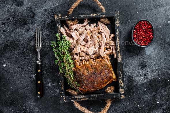Bbq slow roast puilled pork meat in a wooden tray. Black background. Top view