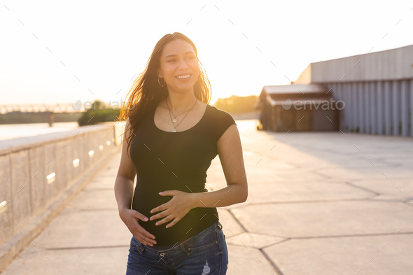 Portrait of a happy pregnant woman looking at side walking on embankment at sunset. Pregnancy and - Stock Photo - Images