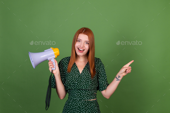 Young red hair woman on green background with megaphone happy excited pointer finger right