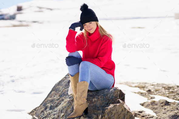 Blonde woman sitting on a rock in the snowy mountains in winter, in Sierra Nevada, Granada, Spain - Stock Photo - Images