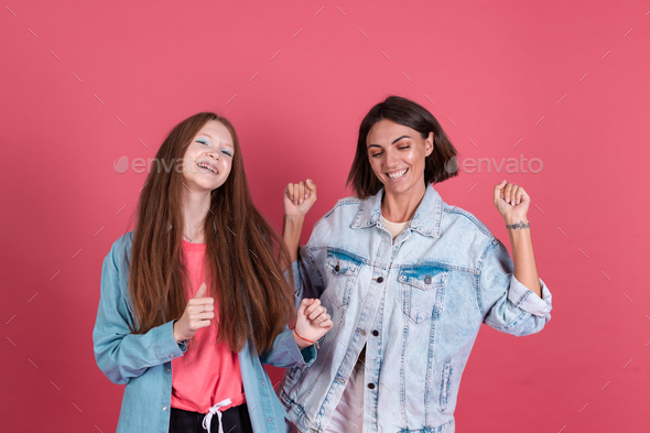 Modern mom and daughter in denim jackets on terracotta background having fun together moving dancing