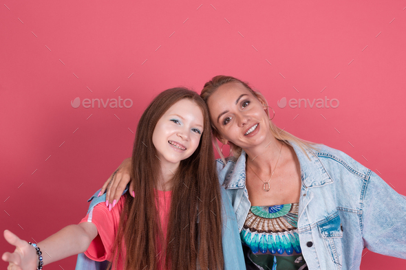 Modern mom and daughter in denim jackets on terracotta background hugging and smiling