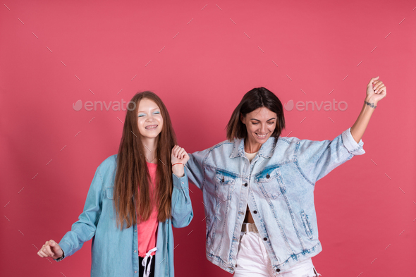 Modern mom and daughter in denim jackets on terracotta background having fun together moving dancing