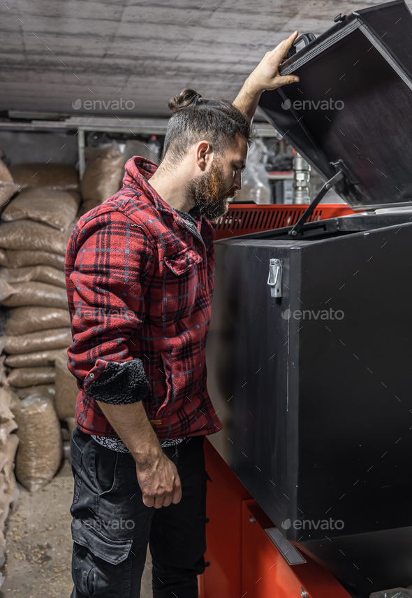 The man looking into a boiler on solid fuel in the room with pellets.