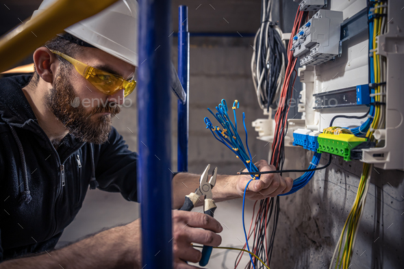 A male electrician works in a switchboard with an electrical connecting cable. - Stock Photo - Images