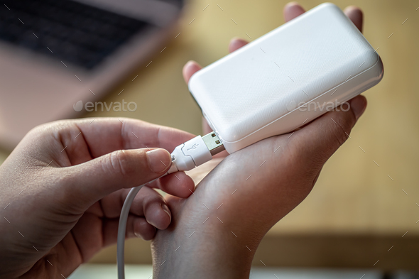 Woman\'s hand holding white USB cable and white power bank.