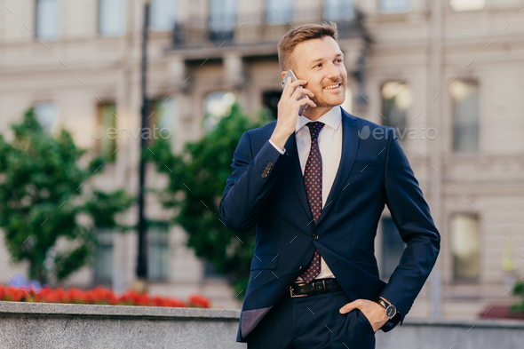 Handsome prosperous young male entrepreneur makes phone call in roaming, uses tariffs - Stock Photo - Images