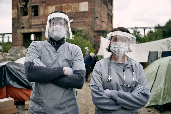 Two clincians in protective workwear standing in refugee camp