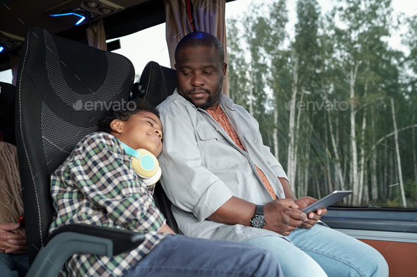 Young African man with tablet looking at his sleeping son