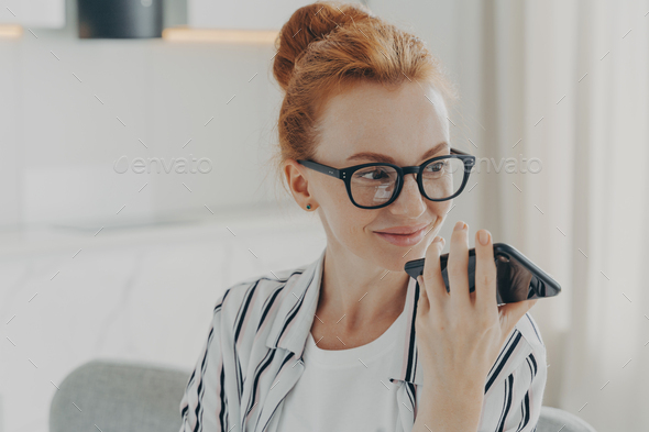 Horizontal shot of ginger woman uses voice assistant on smartphone makes voice call
