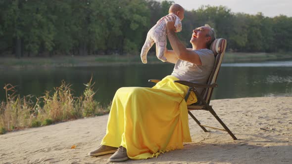 Grandfather Holding Newborn Baby Granddaughter Outdoors alt
