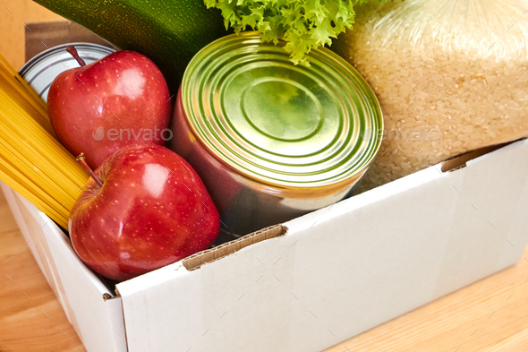 Donation box with vegetables, zucchini, salad, fruits, apples, olive oil, rice, pasta and tin on a