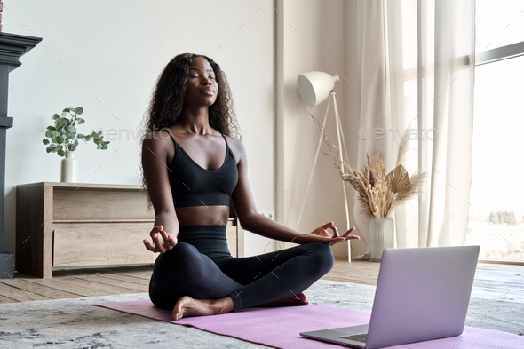 Young calm fit healthy African black woman at home doing yoga learning  online class. Stock Photo by insta_photos