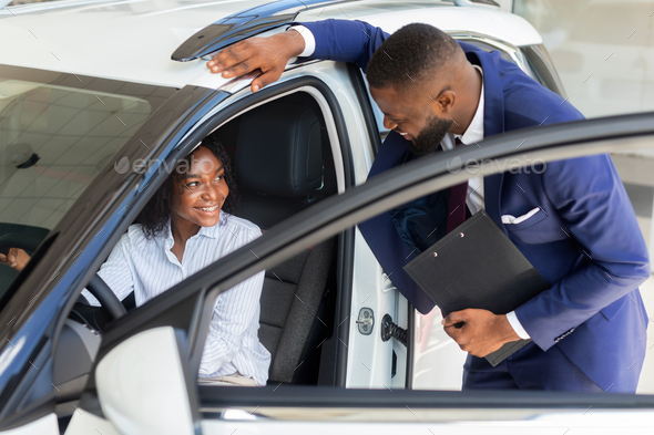 Professional Black Manager In Auto Showroom Consulting Female Client Sitting In Car