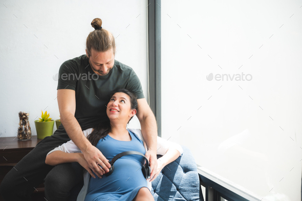 Beautiful young pregnant woman sitting on bed with loving and caring husband trying to connect - Stock Photo - Images