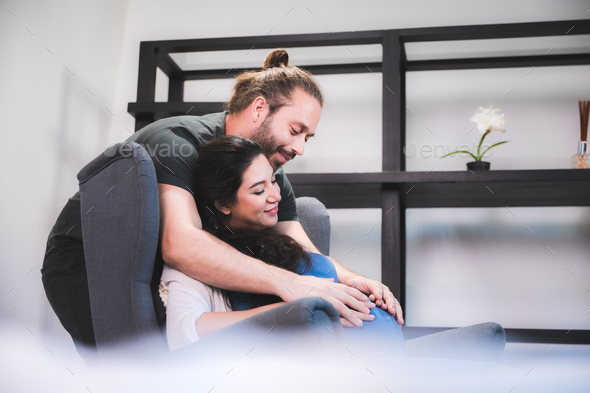 young pregnant woman sitting on bed with loving caring husband trying to connect with baby - Stock Photo - Images