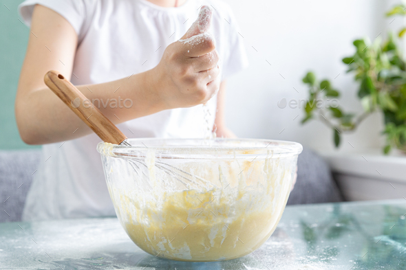 A close-up of the upper body of a child claps its hands over a bowl of wafer dough