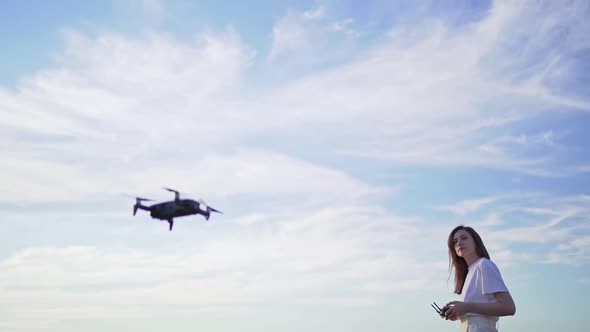 A Woman Controls a Quadcopter, a Beautiful Cloudy Sky in the Background. Drone Takes Off Into the