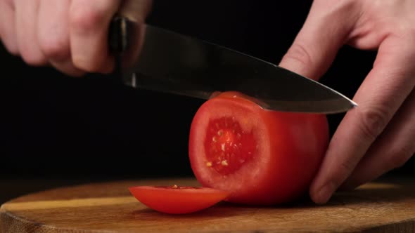 Slicing fresh tomato on wooden the cutting Board. Black background. Close up.4k