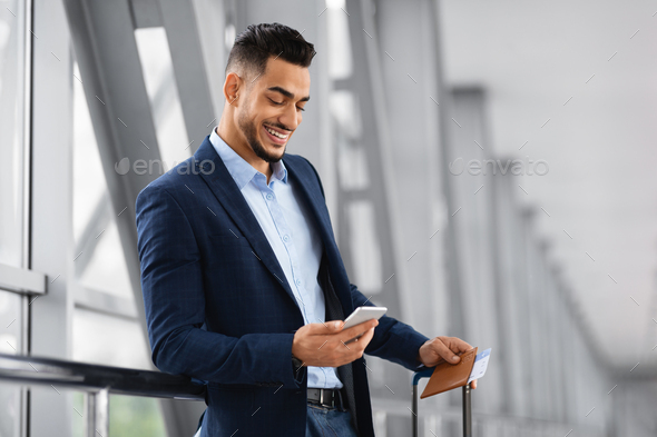 Mobile Roaming. Young Smiling Middle Eastern Businessman Using Smartphone In Airport