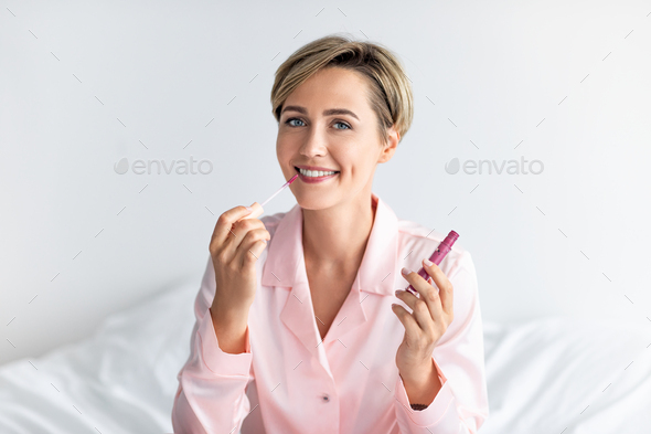 Smiling woman applying lip gloss and looking at camera