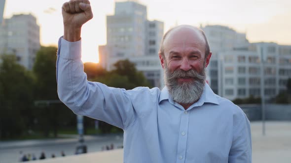 Happy Smiling Contented Grandfather Raises Clenched Fist Waves Hand Shows Gesture of Confidence alt