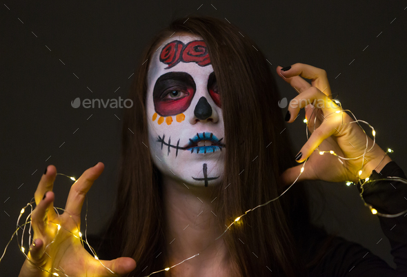 Young woman with creepy face paint holding fairy lights