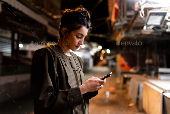 Stylish lady with smartphone on closed market at night