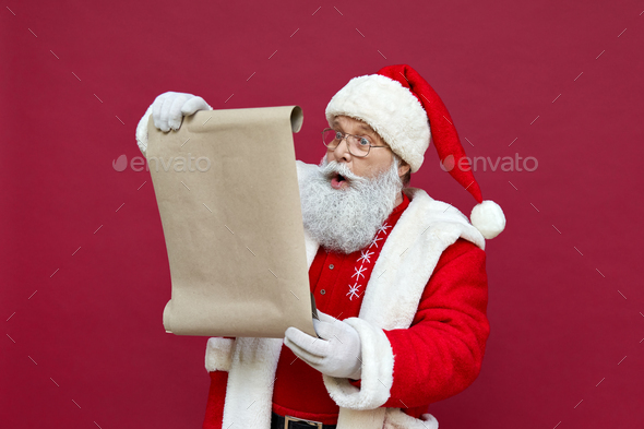 Shocked Santa Claus wearing costume reading wish list on red background.  Stock Photo by insta_photos
