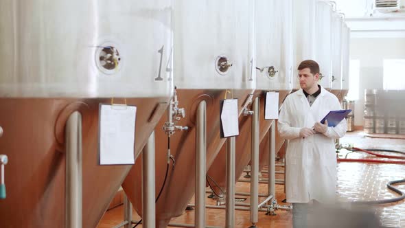 Brewery Worker in a White Coat Supervises the Work