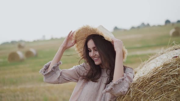 Happy Young Girl Putting Hat on Blowing Hair at Haycock in Windy Field alt