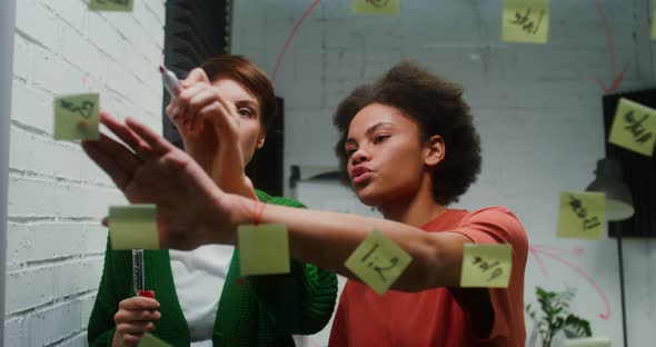 A Woman is Drawing a Business Strategy on a Glass Board Working with Assistant alt