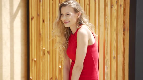 Smiling Woman in Red Dress Standing Near Wooden Wall