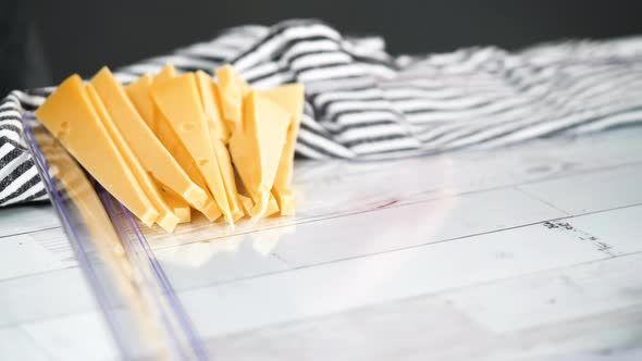 Step by step. Slicing a gourmet cheese on a white cutting board with a kitchen knife. alt