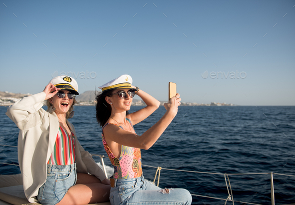 Attractive happy women taking selfie on smartphone on edge of yacht in sea