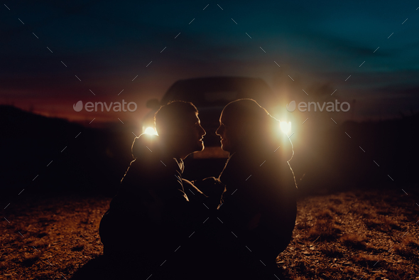 Men hugging and sitting on ground near car on field at night
