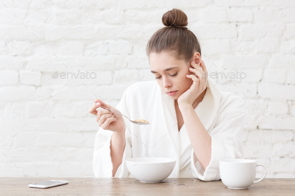 Amazing young bored woman eating breakfast and sitting at wooden table