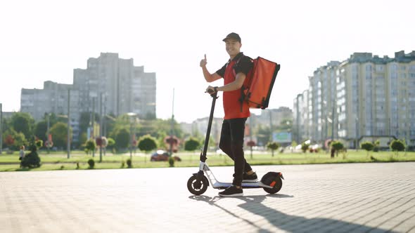 Delivery Man With Red Backpack Appears in the Video on an Electric Scooter and Shows a Thumb Up