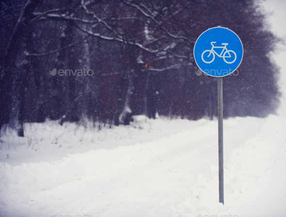 Cycle lane sign covered with snow against a dark forest