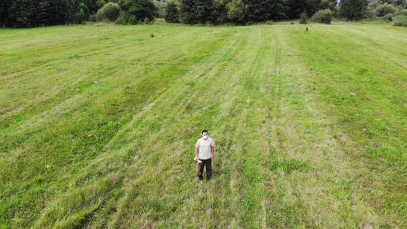 Man in Mask Standing in a Green Field Outside, Aerial Shot From Drone, View From Above