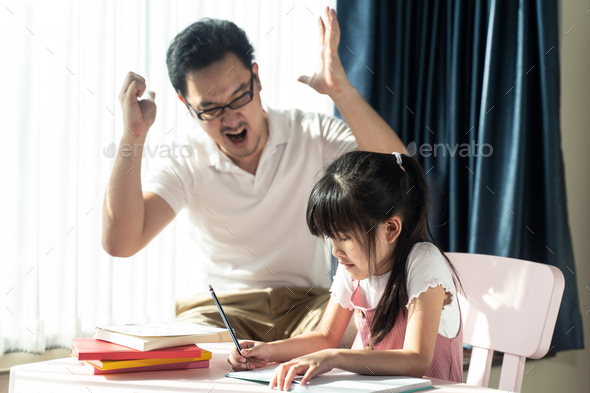 Asian young little girl learning, reading and does homework with mean dad strictly teaching - Stock Photo - Images