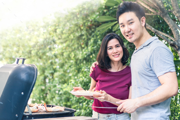 Asian young couple having small party grill lobster, barbecue dinner meal together in garden.