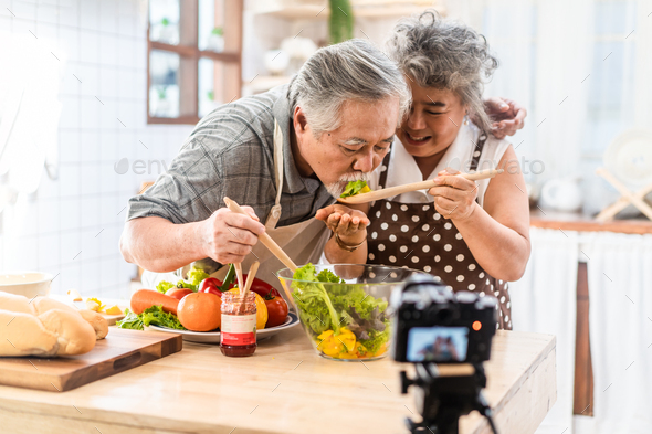 Asian elder senior couple grandparents eating salad dish after cooking recording vlog vdo