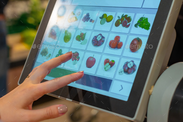 A woman is searching an appropriated fruit product on the screen of electronic balances for weighing
