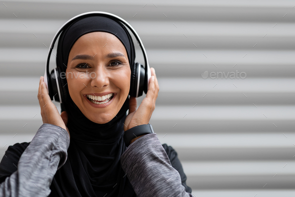Cheerful Muslim Woman In Hijab And Wireless Headphones Listening Music Outdoors - Stock Photo - Images