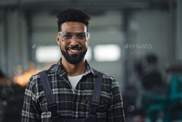 Portrait of young industrial man working indoors in metal workshop, looking at camera