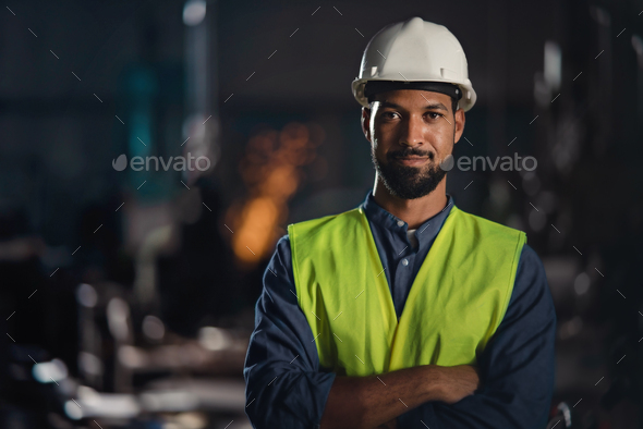 Portrait of happy young industrial man with protective wear indoors in metal workshop, looking at