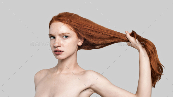 Strong hair. Portrait of young and confident redhead woman holding her long silky hair while