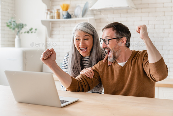 Happy excited mature middle-aged couple celebrating success in business, paying bills, lottery